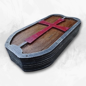 May include: A wooden box with a metal frame and a red cross on the lid. The box is designed to look like a medieval shield.