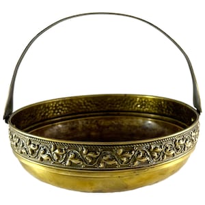 Peut inclure: Un bol en laiton vintage avec une bordure florale décorative et une poignée incurvée. Le bol a une texture martelée à l'intérieur et une finition dorée brillante. La poignée est en métal plus foncé. Ce bol décoratif est parfait pour l'exposition.