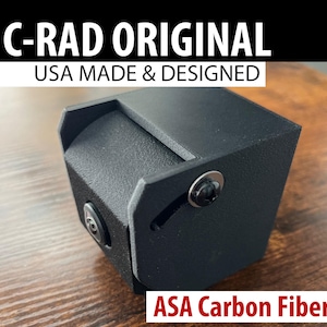 May include: A black, rectangular product with the text "C-RAD ORIGINAL" and "USA MADE & DESIGNED" in white. The product is labeled "ASA Carbon Fiber". The item has a textured surface and is secured with black screws.