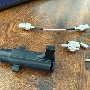 May include: A selection of electronic components, including a black plastic housing, silver connectors, and a cable with a copper wire core. The items are displayed on a wooden surface.