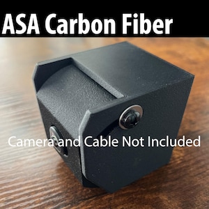 May include: A black camera housing made of ASA carbon fiber. The housing has a hinged door and a screw on the side. The text "Camera and Cable Not Included" is printed on the housing.