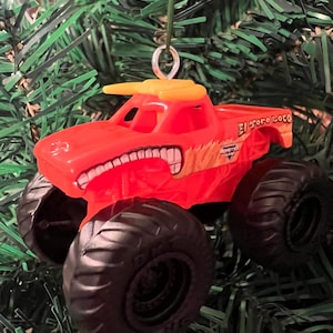 Puede incluir: Adorno navide&ntilde;o de un cami&oacute;n monstruo rojo y amarillo con la inscripci&oacute;n "El Toro Loco". El cami&oacute;n tiene neum&aacute;ticos negros grandes y un dise&ntilde;o de toro en la parte delantera. Cuelga de un hilo verde.