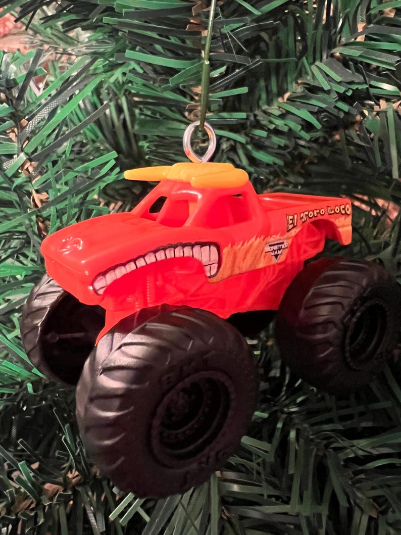 Puede incluir: Adorno navide&ntilde;o de un cami&oacute;n monstruo rojo y amarillo con la inscripci&oacute;n "El Toro Loco". El cami&oacute;n tiene neum&aacute;ticos negros grandes y un dise&ntilde;o de toro en la parte delantera. Cuelga de un hilo verde.