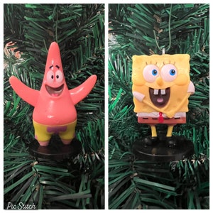 May include: Two Christmas ornaments featuring characters from the cartoon Spongebob Squarepants. The first ornament is a pink starfish with a yellow star on its pants. The second ornament is a yellow square with a brown face and a red tie.