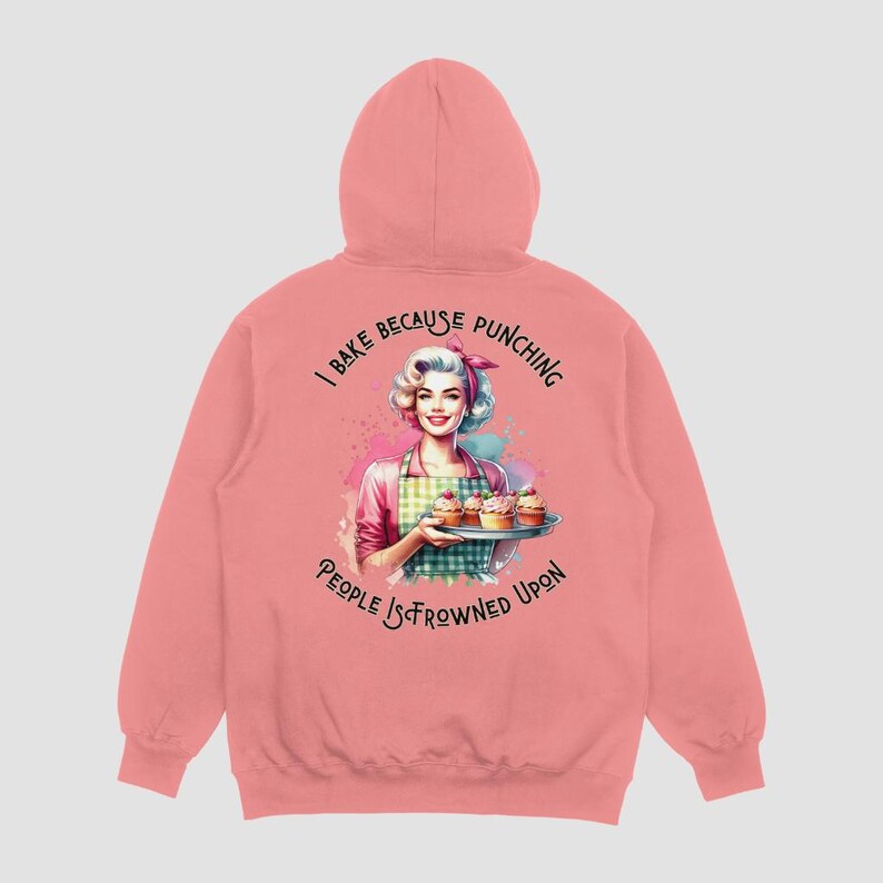 Pu&ograve; includere: Felpa con cappuccio rosa con una stampa grafica di una donna che tiene un vassoio di cupcake. Il testo sulla felpa recita "I bake because punching people is frowned upon."