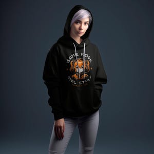May include: Black hoodie with a graphic print of an anime girl wearing headphones and a face mask. The graphic text reads "Game Mode Girl Style Feral But Cute".