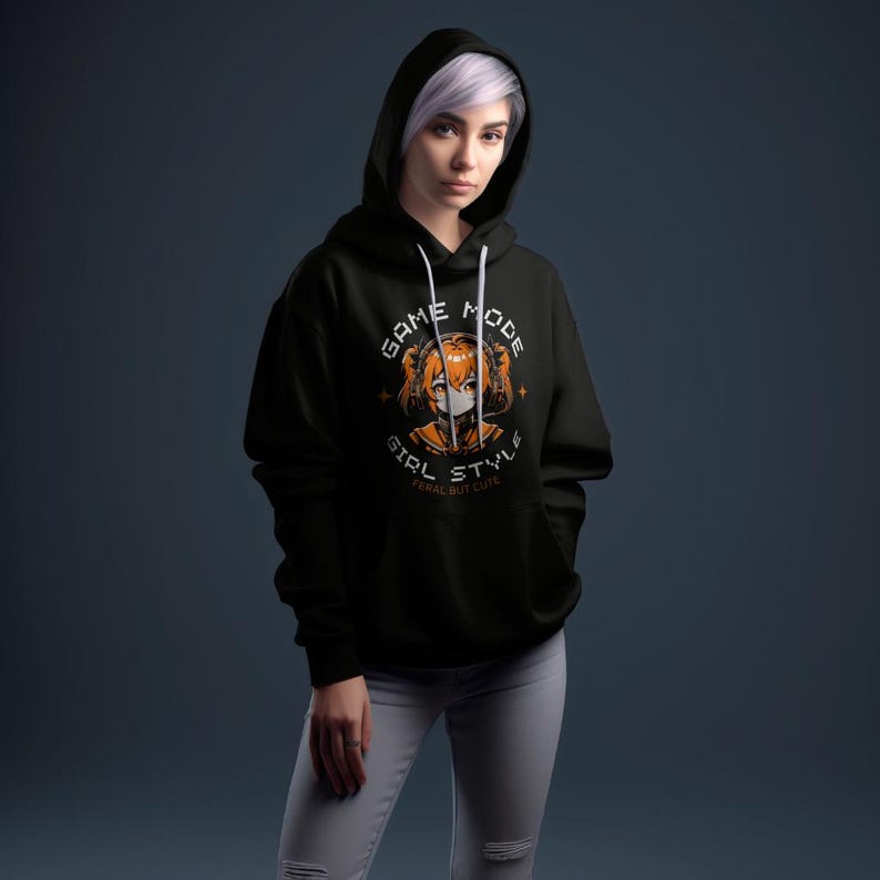 May include: Black hoodie with a graphic print of an anime girl wearing headphones and a face mask. The graphic text reads "Game Mode Girl Style Feral But Cute".
