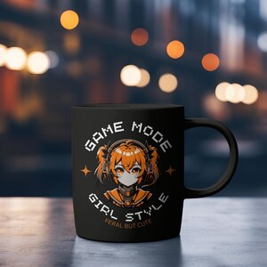 May include: Black ceramic mug with a white and orange design. The design features a cartoon anime girl with headphones and the text "GAME MODE GIRL STYLE FERAL BUT CUTE".