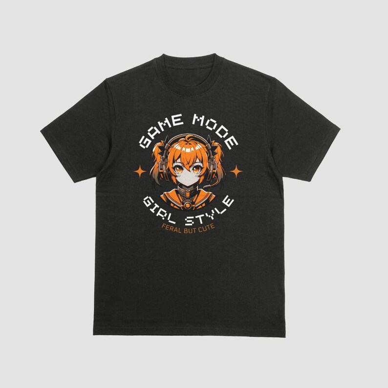 May include: Black t-shirt with a graphic of a girl with orange hair wearing headphones and a black and orange outfit. The graphic is surrounded by a circle with the text "GAME MODE GIRL STYLE FERAL BUT CUTE".