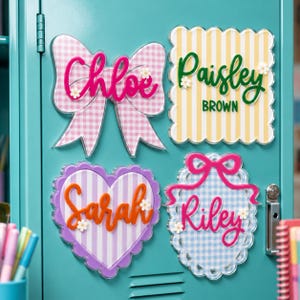 May include: Four decorative acrylic name plaques with scalloped edges and bow accents. The plaques feature pink gingham, yellow stripes, purple stripes, and blue gingham patterns with the names Chloe, Paisley Brown, Sarah, and Riley in raised script.