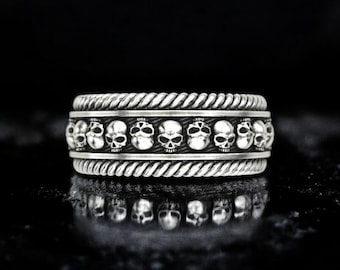 May include: A silver ring featuring a rope-like design and a row of skull details.