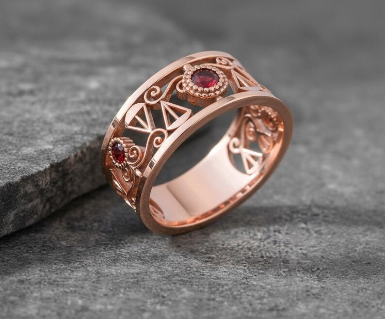 May include: Rose gold ring with intricate filigree design and two red gemstones. The ring features openwork patterns and geometric shapes, showcasing a blend of elegance and artistry. The gemstones are round and set in a bezel setting.