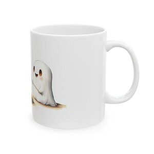 Puede incluir: Taza de caf&eacute; de cer&aacute;mica blanca con una ilustraci&oacute;n de dibujos animados de dos fantasmas amigables tom&aacute;ndose de la mano. Los fantasmas son blancos con ojos negros y sonrisas.