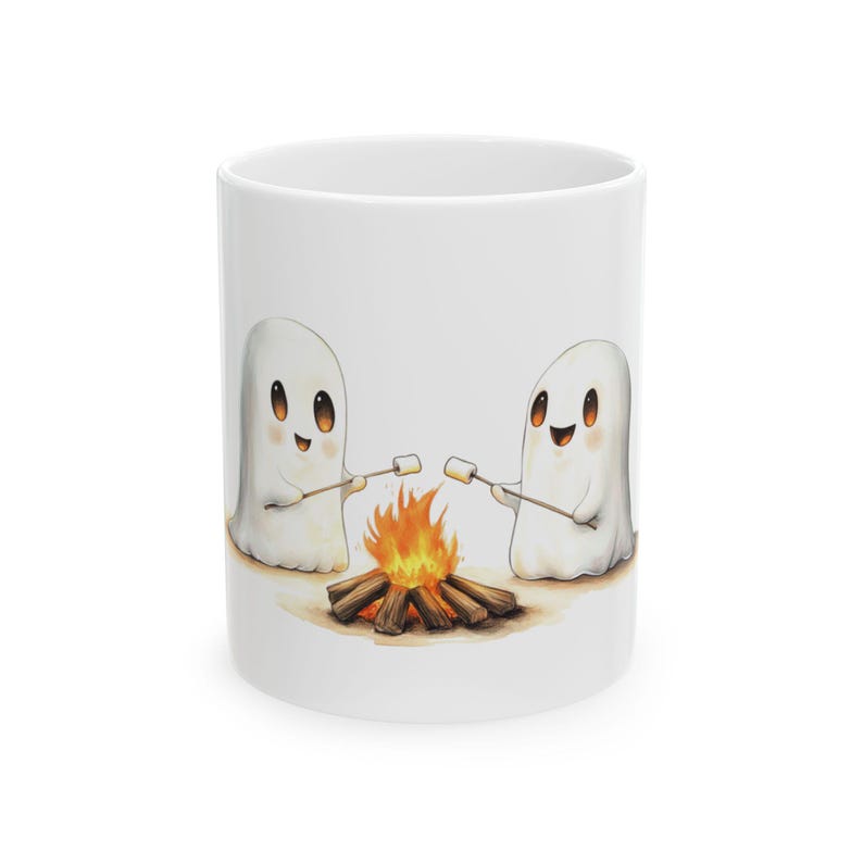 Puede incluir: Taza de cer&aacute;mica blanca con una ilustraci&oacute;n de dibujos animados de dos fantasmas asando malvaviscos sobre una fogata. Los fantasmas son blancos con ojos negros y bocas sonrientes.