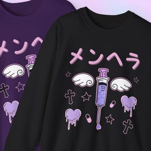Könnte beinhalten: Zwei Sweatshirts, eines lila und eines schwarzen, mit einem Kawaii-Design. Das Design umfasst japanischen Text, eine Spritze, Wolken, Sterne, Herzen und Kreuze in Lila- und Weißtönen.