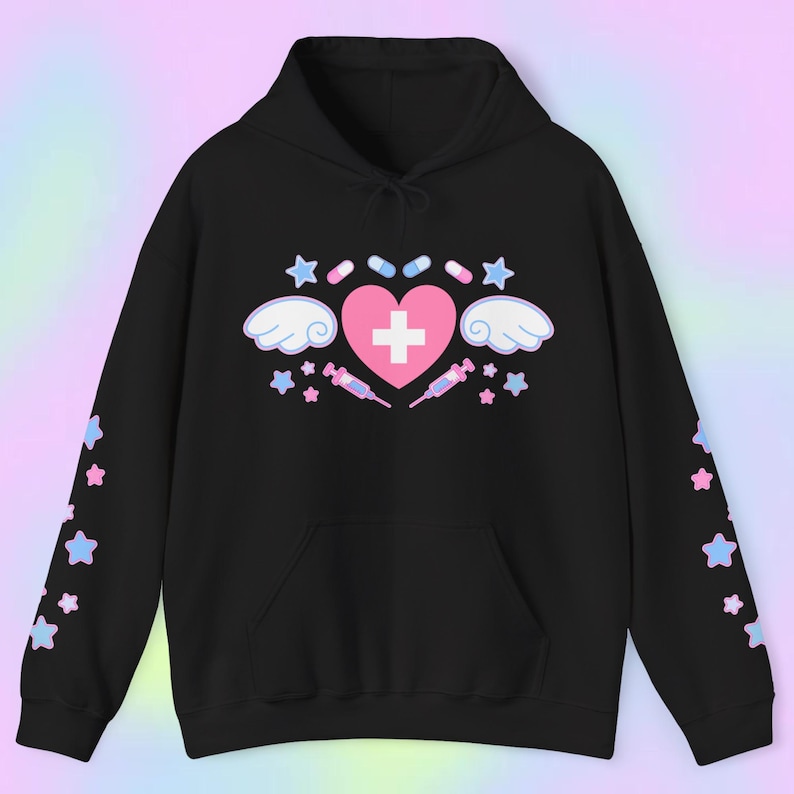 Pode incluir: Moletom preto com um cora&ccedil;&atilde;o rosa, uma cruz branca, asas, estrelas, p&iacute;lulas e seringas. As mangas t&ecirc;m estrelas azuis e rosas. O moletom tem capuz e um bolso frontal.