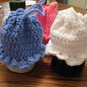 May include: Three crocheted jar covers in blue, pink, and white. Each cover has a ruffled edge and a crocheted design.