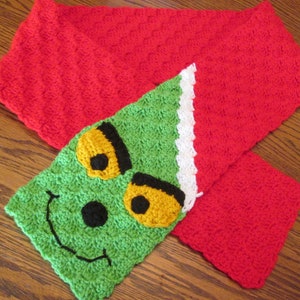 May include: A green crocheted scarf with a Grinch face on it. The scarf is red and white on the edges.