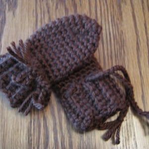 May include: A brown knitted fingerless glove with a long fringe. The glove is made of a soft, textured yarn.