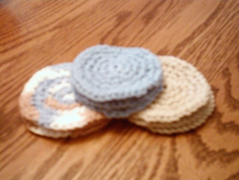 Peut inclure: Trois dessous-de-verre en crochet, un bleu, un blanc &agrave; rayures brunes et un beige. Les dessous-de-verre sont empil&eacute;s les uns sur les autres.