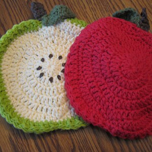 May include: Two crocheted pot holders shaped like apples. One is red and the other is white with a green stem and leaf.