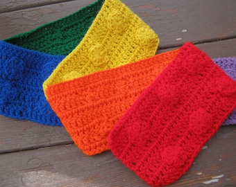 Peut inclure: Une écharpe en crochet arc-en-ciel avec un motif texturé et des bosses surélevées. L'écharpe est faite dans des tons de vert, jaune, orange, rouge et violet.