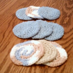 Peut inclure: Un ensemble de dessous-de-verre en crochet dans diff&eacute;rentes nuances de bleu, beige et blanc. Les dessous-de-verre sont circulaires et ont une surface textur&eacute;e.