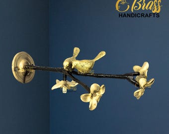 May include: A brass wall decor piece featuring a branch with two birds and flower accents. The branch is black, and the birds and flowers are gold. The Brass Handicrafts logo is in the upper right corner.