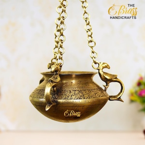 May include: A gold hanging oil lamp with intricate floral designs and two bird-shaped handles. The lamp is suspended by a chain and has a round, slightly curved body.