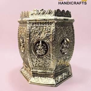 Könnte beinhalten: Ein goldfarbenes, sechseckiges Messinghandwerk mit aufwendigen Blumen- und Gottheitsschnitzereien. Das Stück hat einen dekorativen Rand und Sockel, mit dem Text "THE Brass HANDICRAFTS" in goldener Schrift.