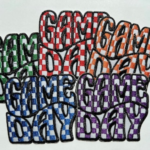 May include: Embroidered patches in various colors, each featuring the words "GAME DAY" in a bold, checkered design. The patches include green, red, orange, blue, and purple color schemes, all with a black outline.