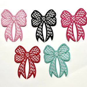 May include: Five checkered fabric bows in different colors: pink, black, red, turquoise, and light blue. The bows are all the same size and shape, with a checkered pattern.