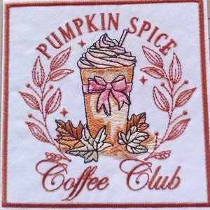 Puede incluir: Parche bordado con una taza de café marrón y blanca con un lazo rosa y el texto "Pumpkin Spice Coffee Club" en letras marrones.