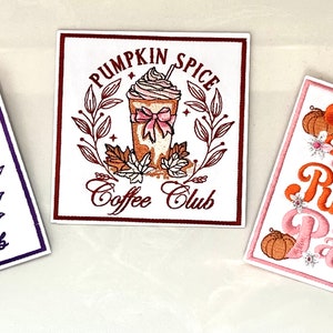 May include: Three square stickers with white backgrounds. The left sticker features purple text reading SALEM WITCH Cocktail Club with three cocktails. The center sticker has brown text PUMPKIN SPICE Coffee Club with a drink. The right sticker says Take me to the PUMPKIN Patch in orange and pink with pumpkins.
