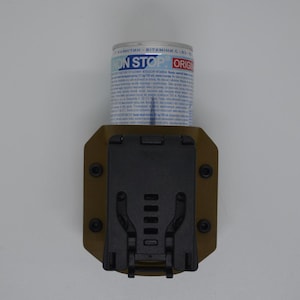 May include: A tan-colored tactical pouch with a black clip and a cylindrical container. The container has blue and white text that reads "NON STOP ORIG". The pouch is designed to hold the container securely.