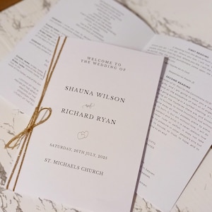 May include: A wedding program with the names Shauna Wilson and Richard Ryan, tied with twine. The program includes the date, July 26th, 2025, and the church name, St. Michael's Church. Additional pages with text are visible.