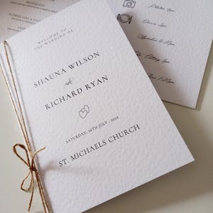 Pode incluir: Programa de casamento com os nomes Shauna Wilson e Richard Ryan, datado de 26 de julho de 2025. O programa é amarrado com barbante e apresenta um símbolo de coração. O texto "Welcome to the Wedding of" está no topo.