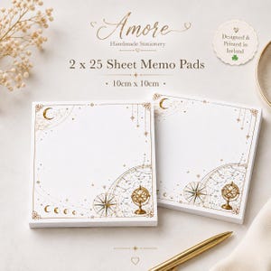 May include: Two square memo pads with 25 sheets each, measuring 10cm x 10cm. The white paper features gold celestial illustrations including a crescent moon, stars, constellations, a compass rose, and an armillary sphere in the corners.