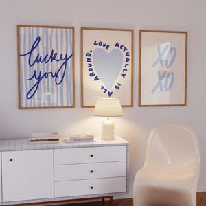 May include: Three framed art prints with wooden frames. The prints feature blue text and designs on a white background. One says "lucky you", another has a heart and says "Love actually is all around", and the last says "XO XO".