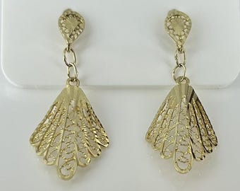 May include: A pair of gold-colored filigree earrings. Each earring features a teardrop-shaped top connected by a chain to a fan-shaped bottom. The fan design has an open, intricate pattern. The earrings are displayed against a white background.