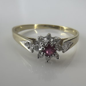 May include: A gold ring with a floral design. The ring features a central pink gemstone surrounded by smaller white stones. The band is gold, and the setting is silver-coloured.
