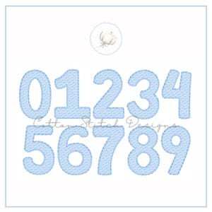 May include: A set of light blue embroidered numbers from 0 to 9, with a denim-like texture. The numbers are displayed on a white background, with the text "Cotton Stitch Designs" below the numbers. A small floral design is at the top.