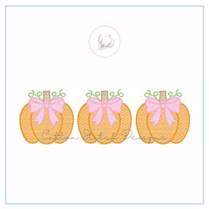 May include: Three embroidered pumpkins with pink bows and green vines. The pumpkins are orange with a textured appearance. The text "Cotton Stitch Designs" is visible on the pumpkins. A small cotton flower design is at the top.