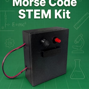 May include: A black rectangular Morse Code STEM Kit device featuring a red LED light, a black push-button switch, and a rectangular black panel. Two red and black wires extend from the side of the unit, which is set against a green background.