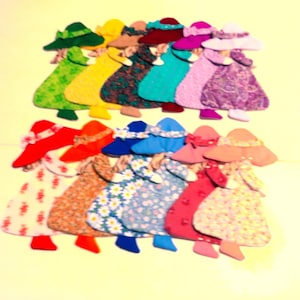 May include: A collection of twelve fabric appliques shaped like figures wearing wide-brimmed hats and dresses. The figures feature various colors including green, yellow, dark brown, teal, purple, white, red, orange, blue, and pink with floral patterns.