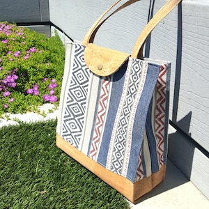 May include: A blue and white striped tote bag with cork accents. The bag has a geometric pattern and is made of canvas.