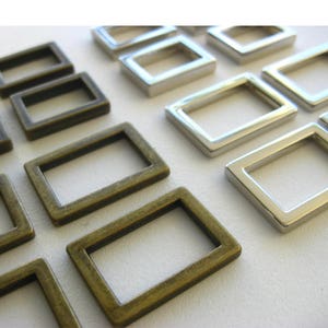 May include: A close-up of two sets of metal rectangular rings. One set is silver and the other is a darker bronze color. The rings are arranged in a staggered pattern.