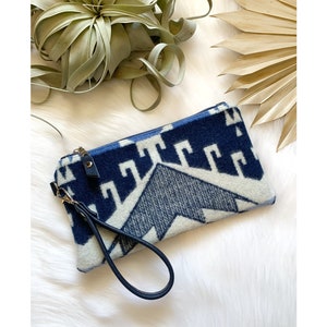 Puede incluir: Un embrague estampado en azul y blanco con una correa negra y un tirador de cremallera dorado.