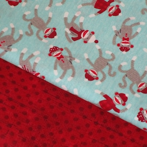May include: A textile featuring a pattern of gray sock monkeys wearing red hats and bow ties on a light blue background. A red fabric with a polka dot pattern is visible in the foreground.