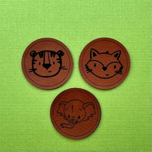 May include: Three brown leather coasters with black animal illustrations. The coasters feature a tiger, a fox, and an elephant.